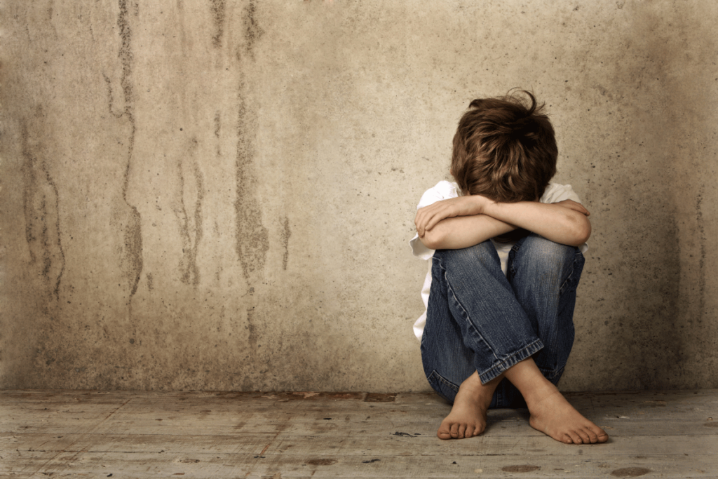 abused barefoot child sitting in corner of empty and dirty room