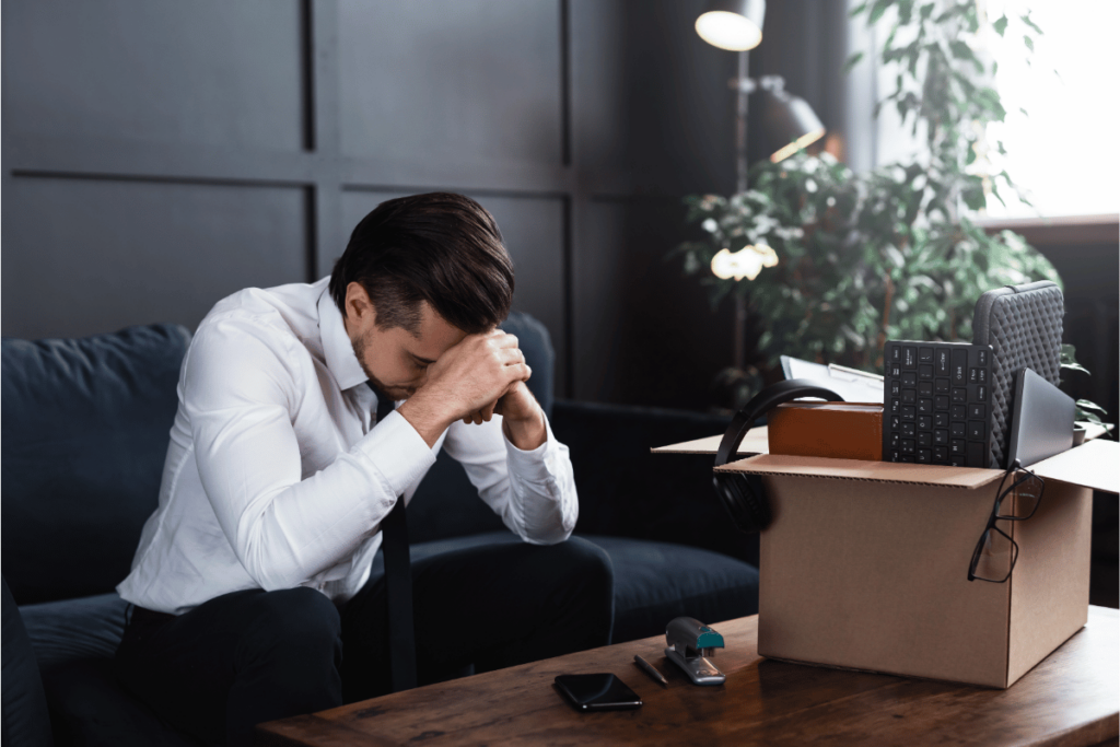 young man with head in his hands and belongings in a box after being fired from his job